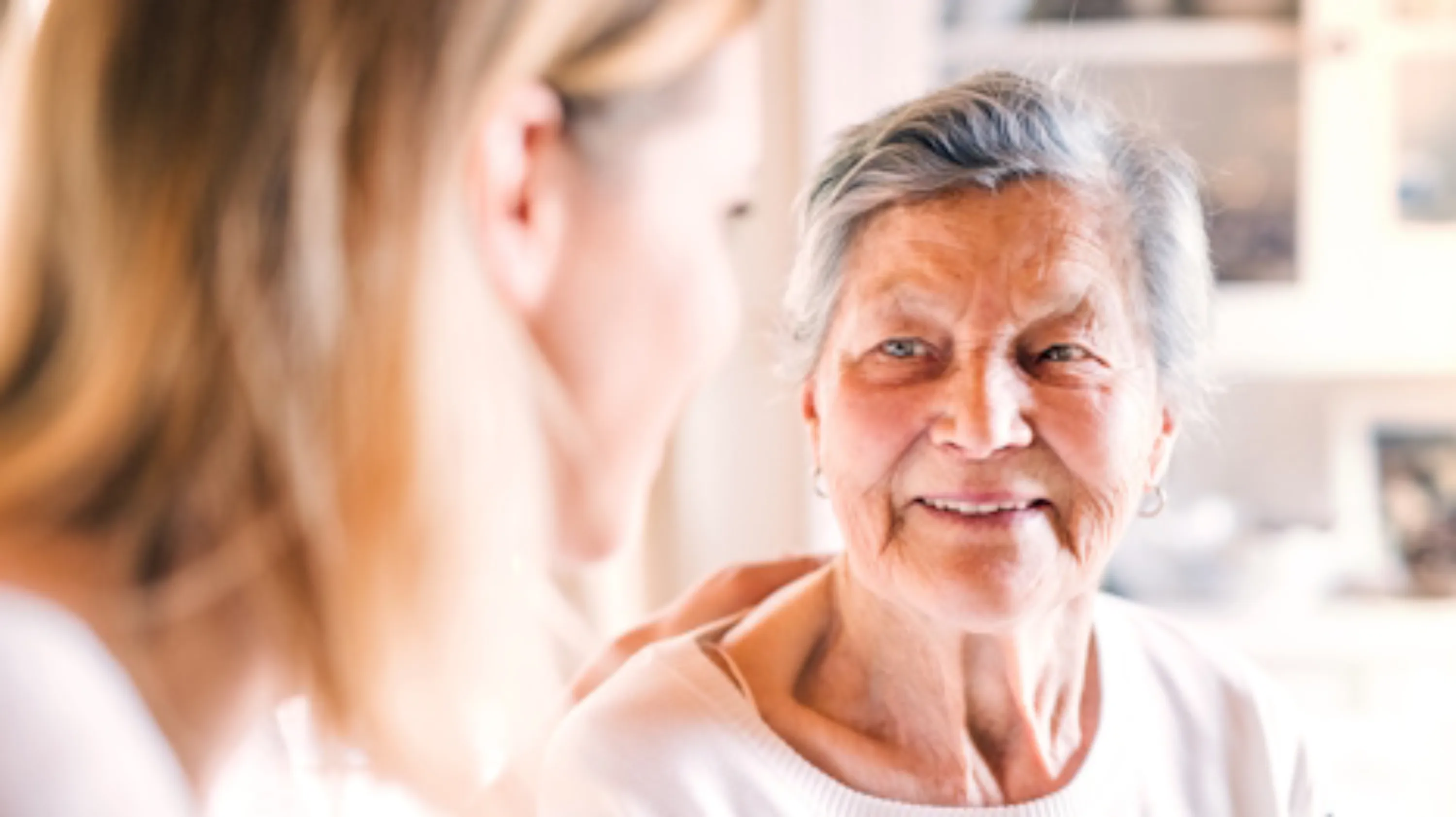 Femme âgée souriante écoutant une femme plus jeune dans un moment complice.