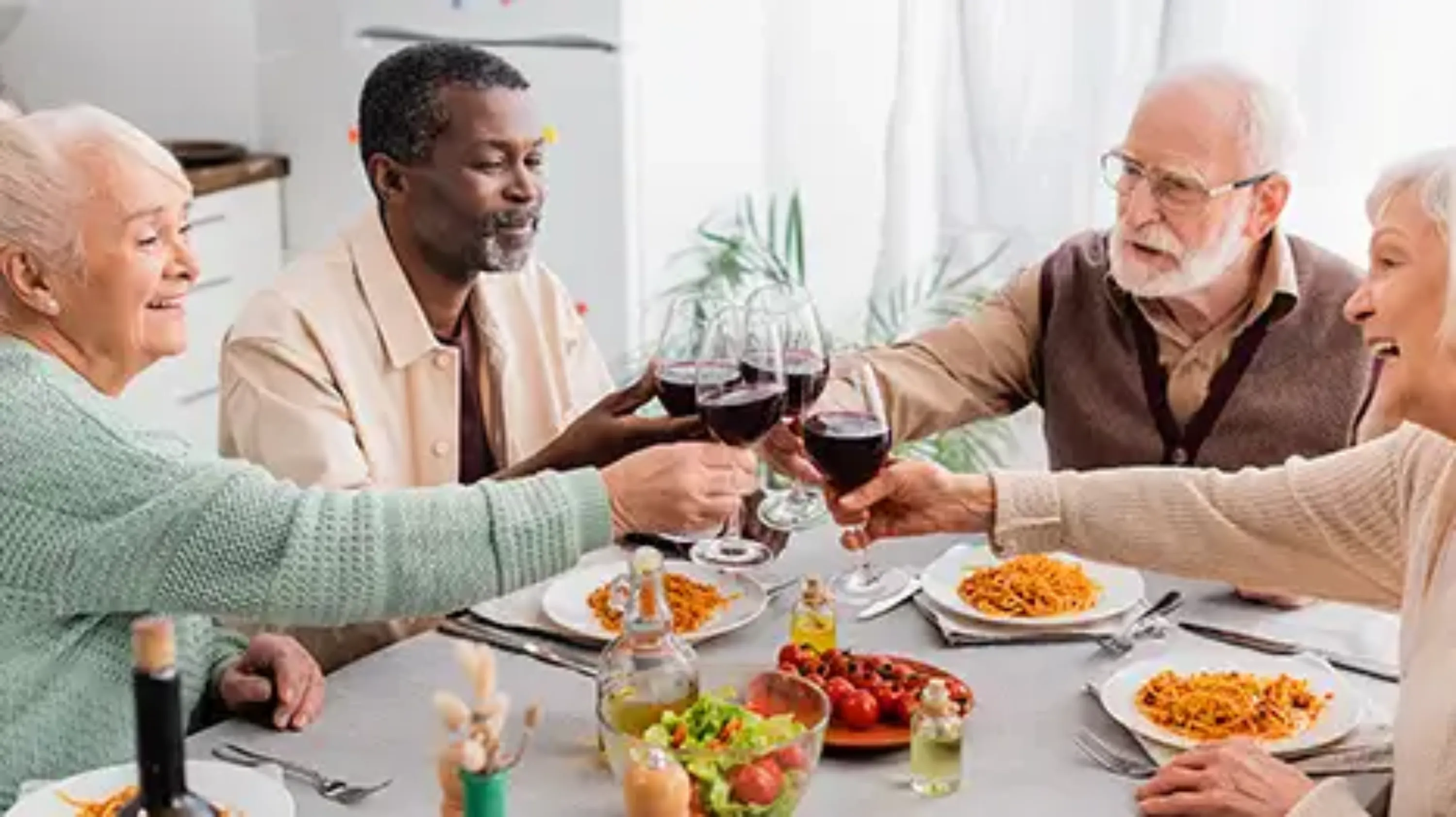 4 personnes âgées pendant un repas, qui trinquent avec des verres de vin