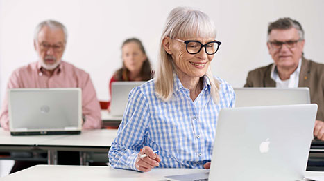 Una donna anziana con gli occhiali è seduta al computer nel suo studio.